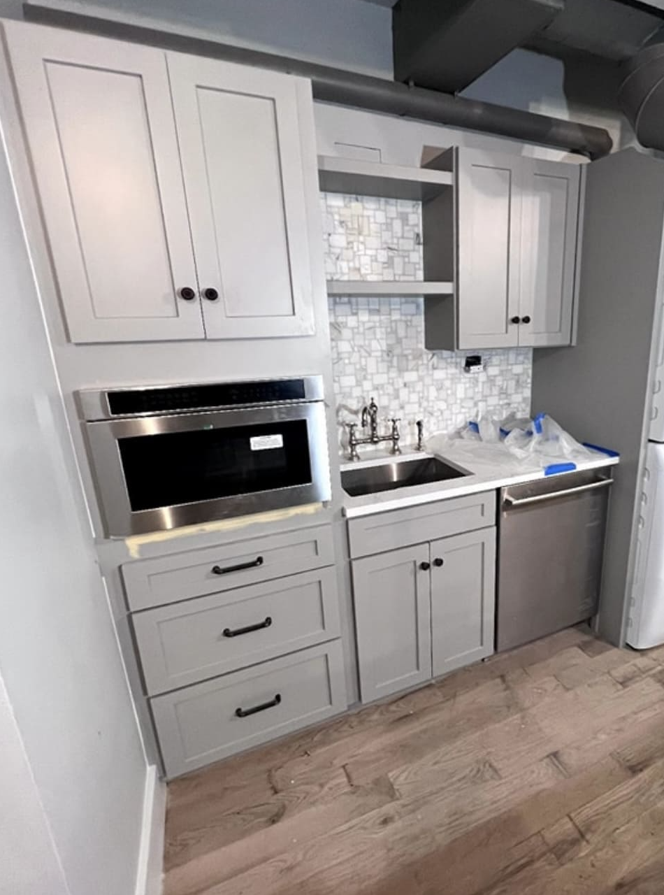 Basement kitchenette with shaker cabinets, wall oven and mosaic backsplash